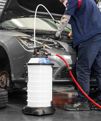 Mechanic using a fluid extractor on a car in a workshop.