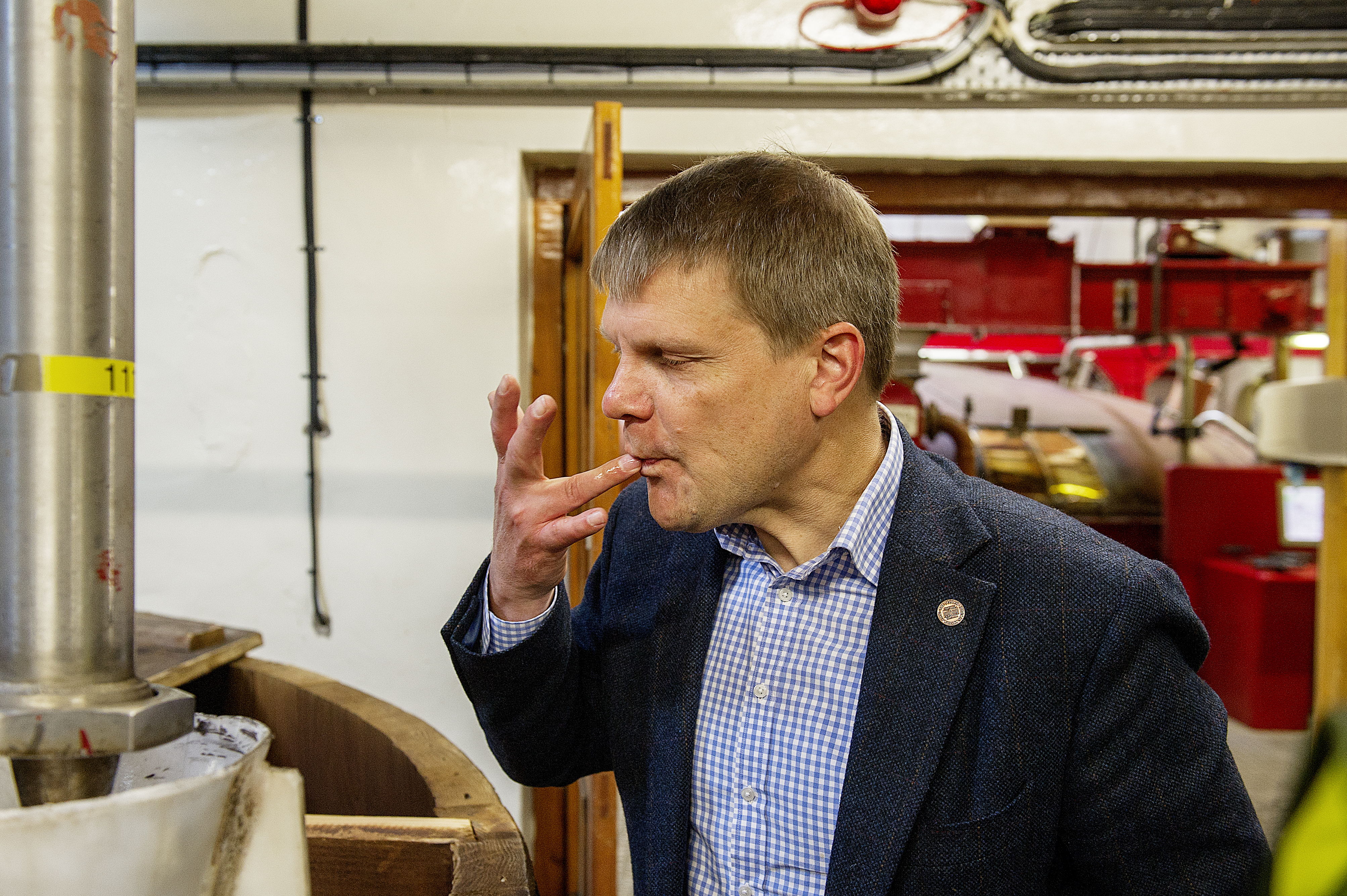Man tasting something in a workshop, surrounded by machinery and equipment.