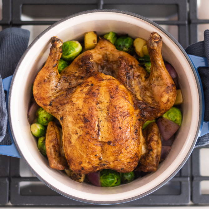 Uncovered Blue Misen Dutch Oven seen from above on a stovetop. A roast chicken with vegetables is visible inside.