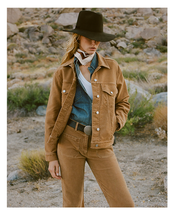 Woman in a brown outfit and hat, standing in a rocky landscape.