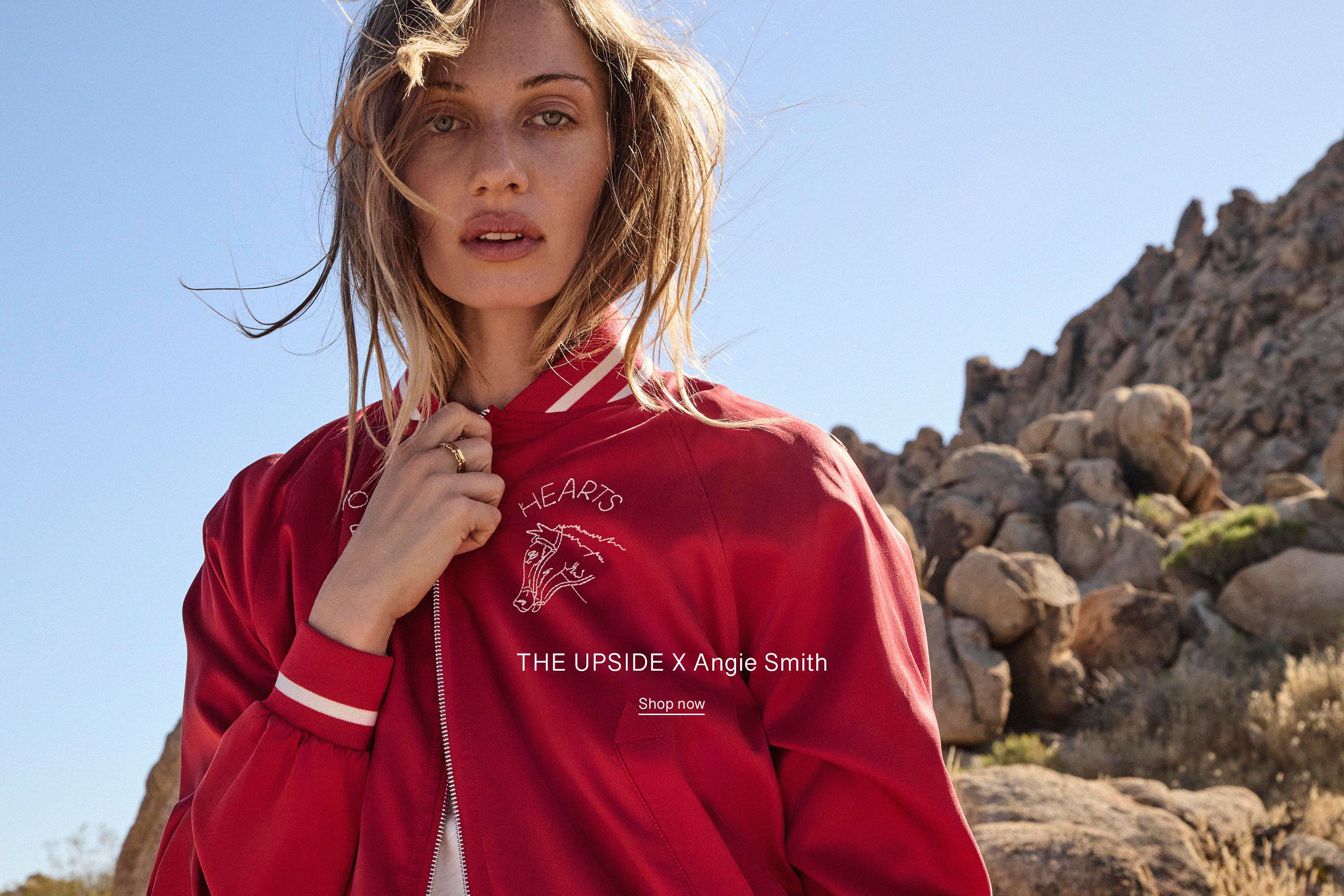 Woman in a red jacket posing outdoors with rocky background.