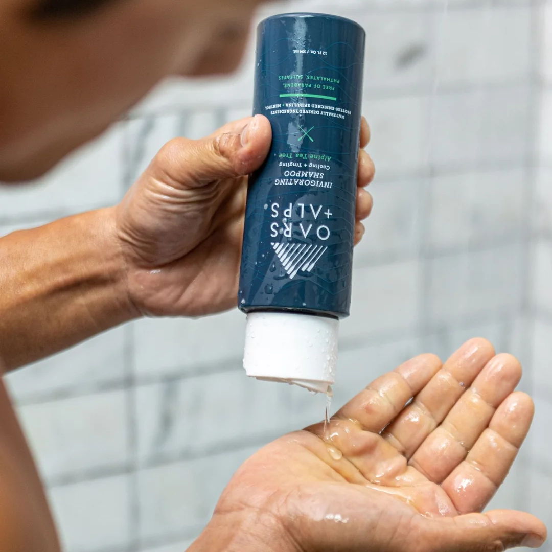 Person applying liquid from a bottle into their hand in a bathroom setting.