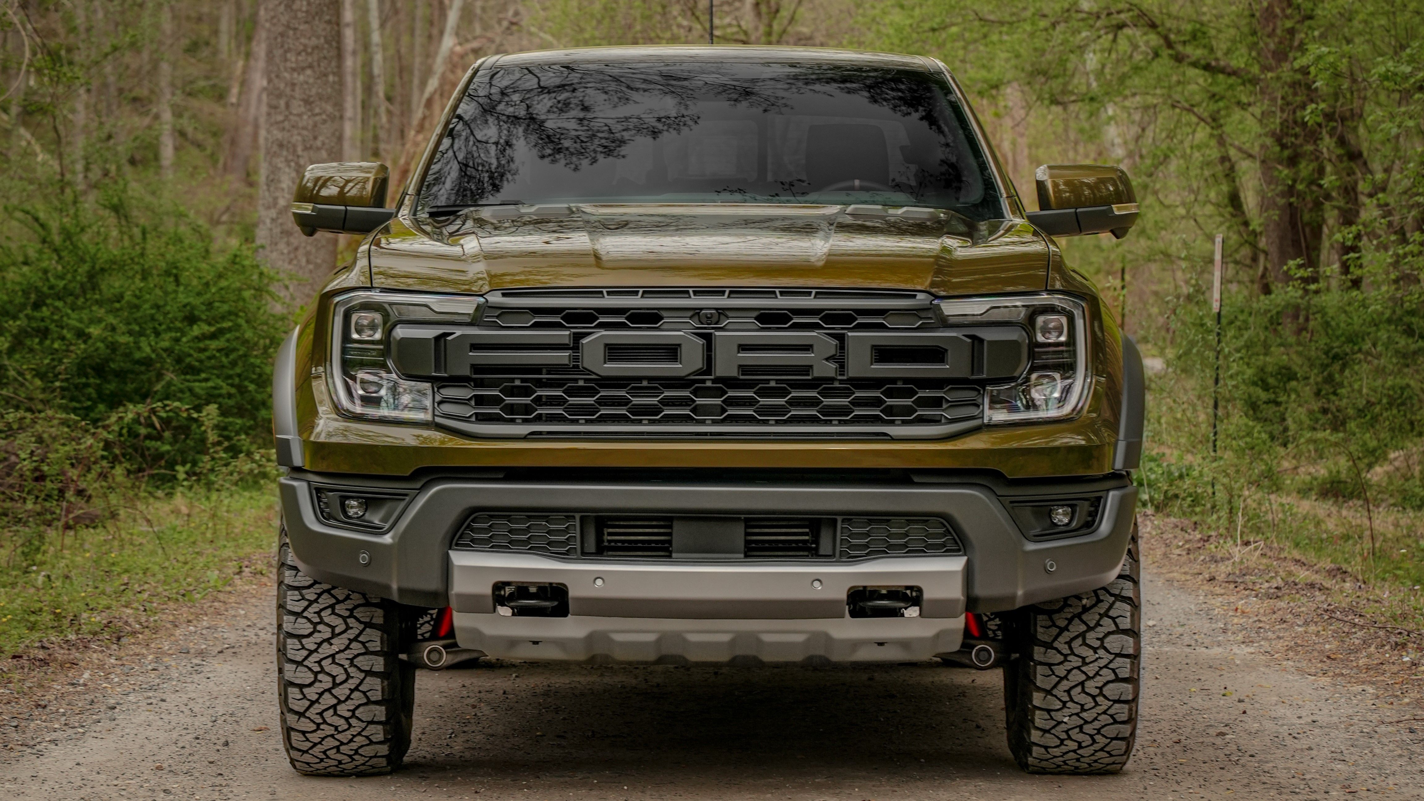 Front view of a green Ford Ranger Raptor on a dirt road.