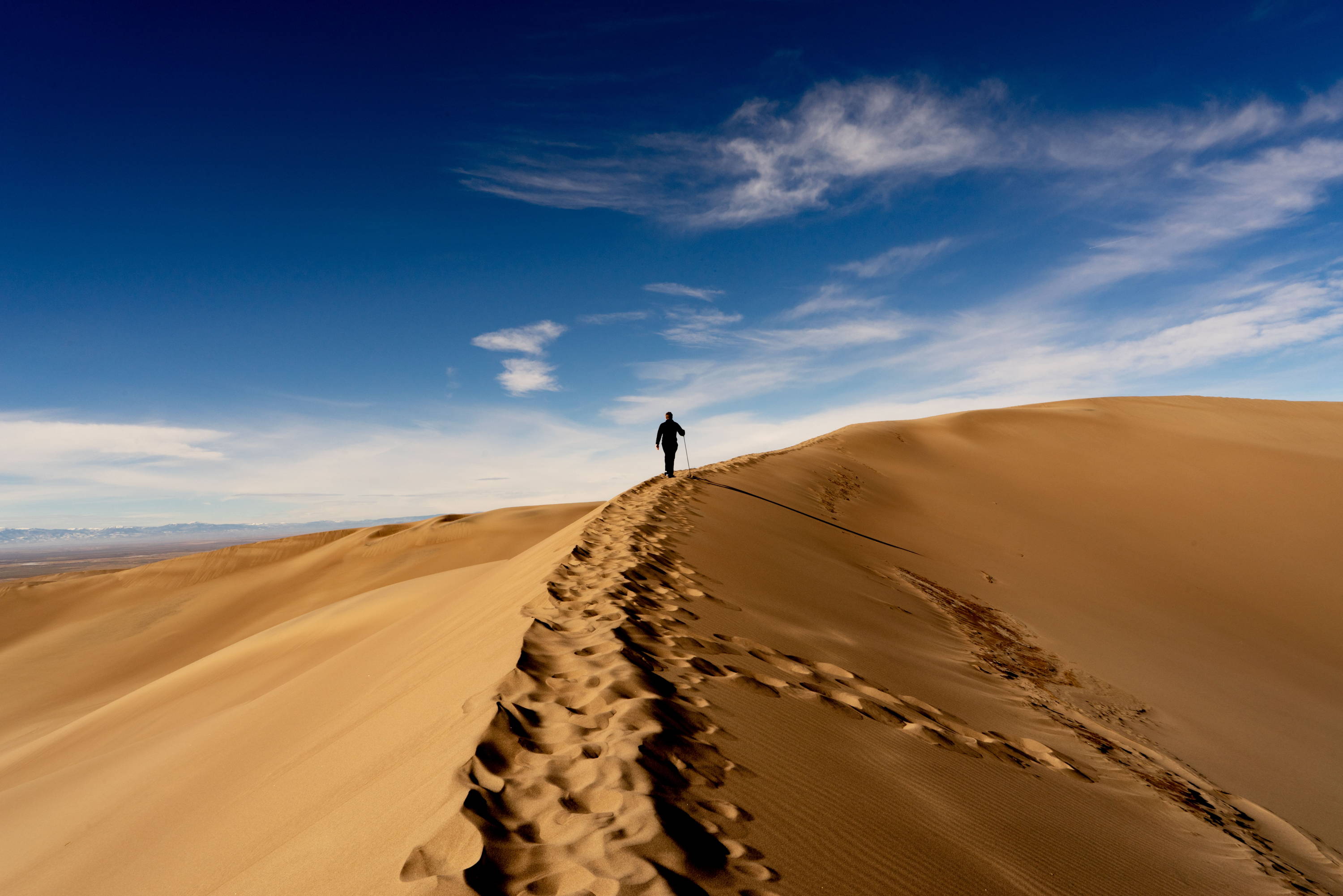 Least Visited National Parks You Need to See: Person hikes atop sand dune into the horizon at Sand Dunes National Park in Colorado.