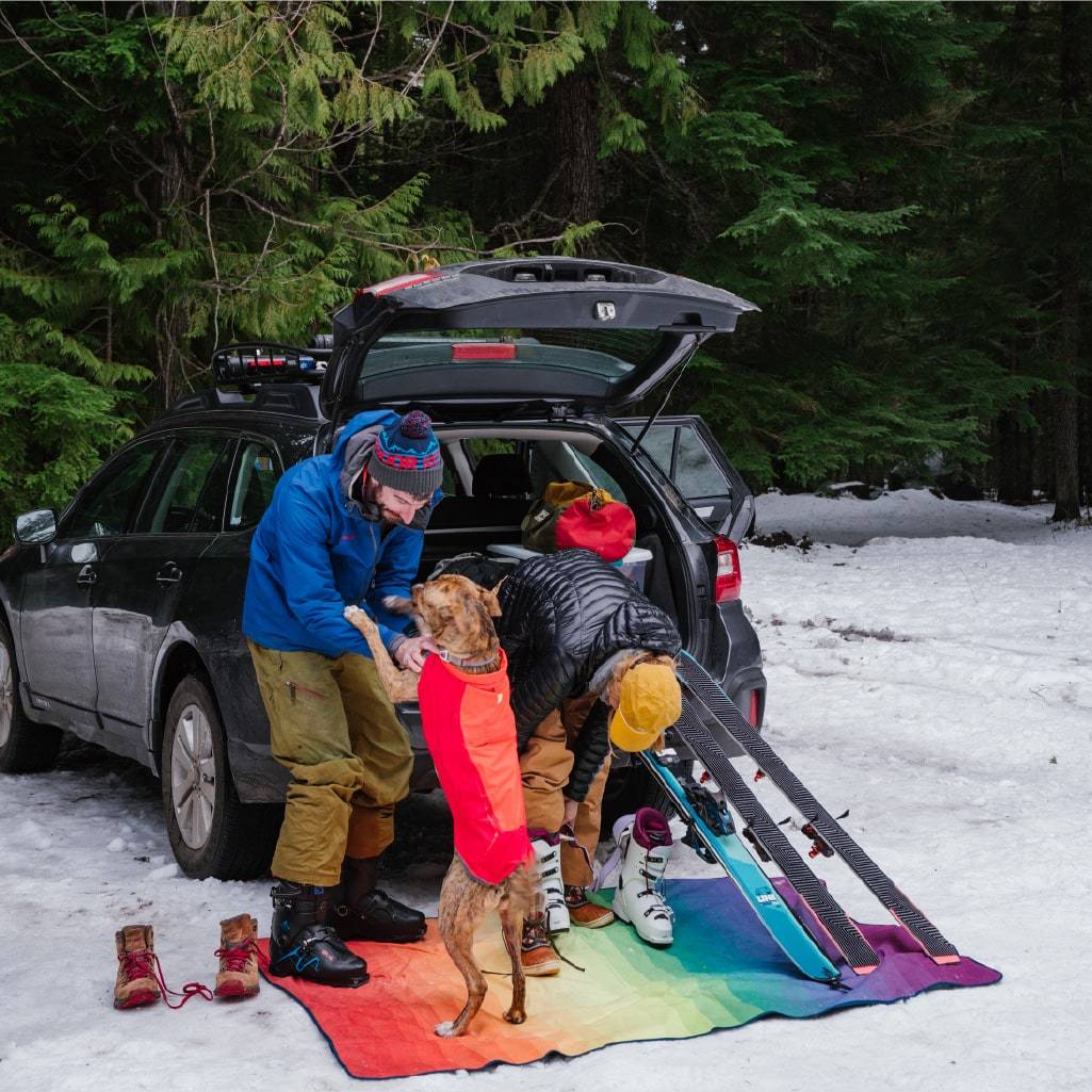 Two people in a ski parking lot getting on their boots on waterproof Rumpl stash mat