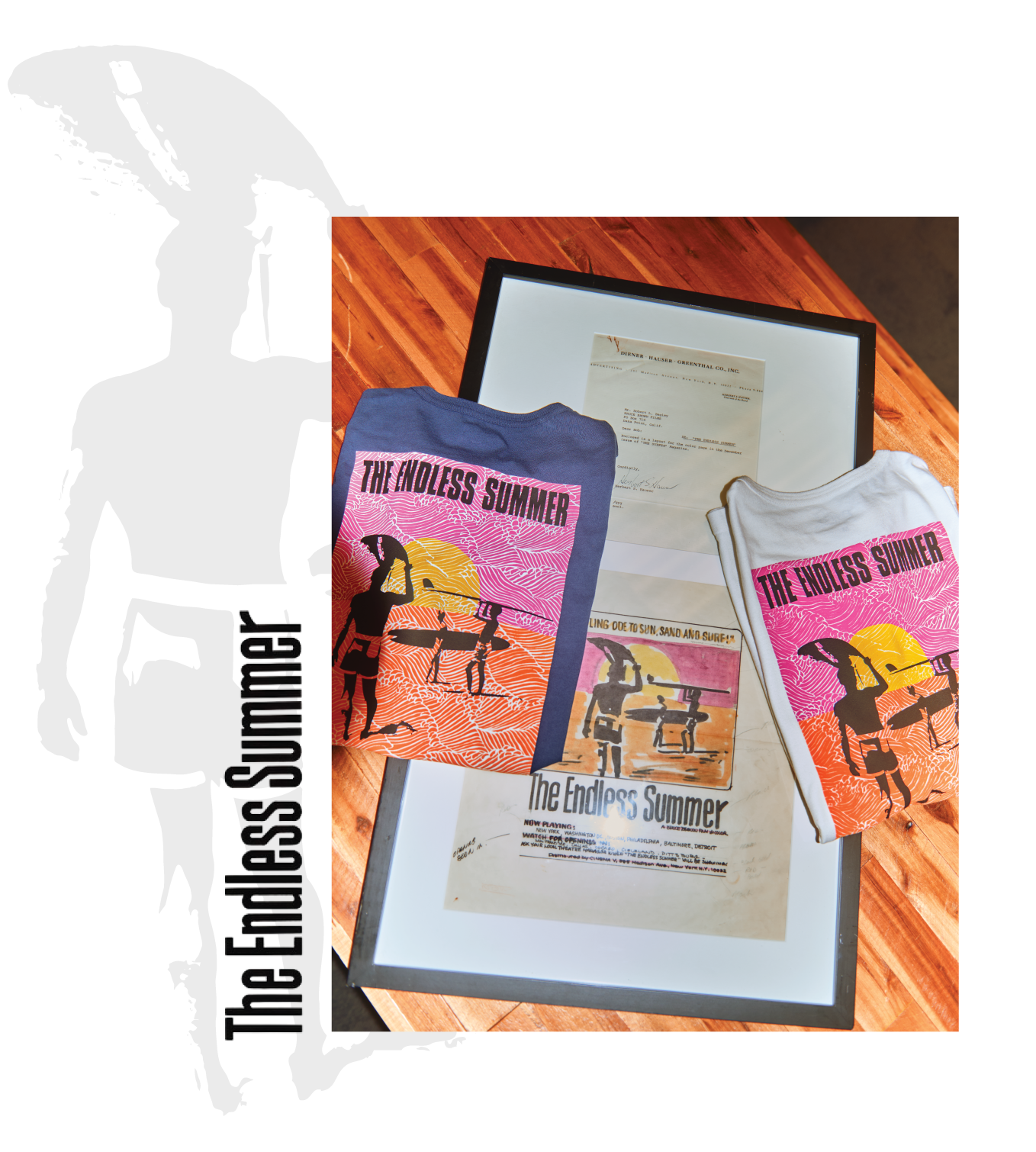 Two t-shirts and a framed poster on a wooden surface.