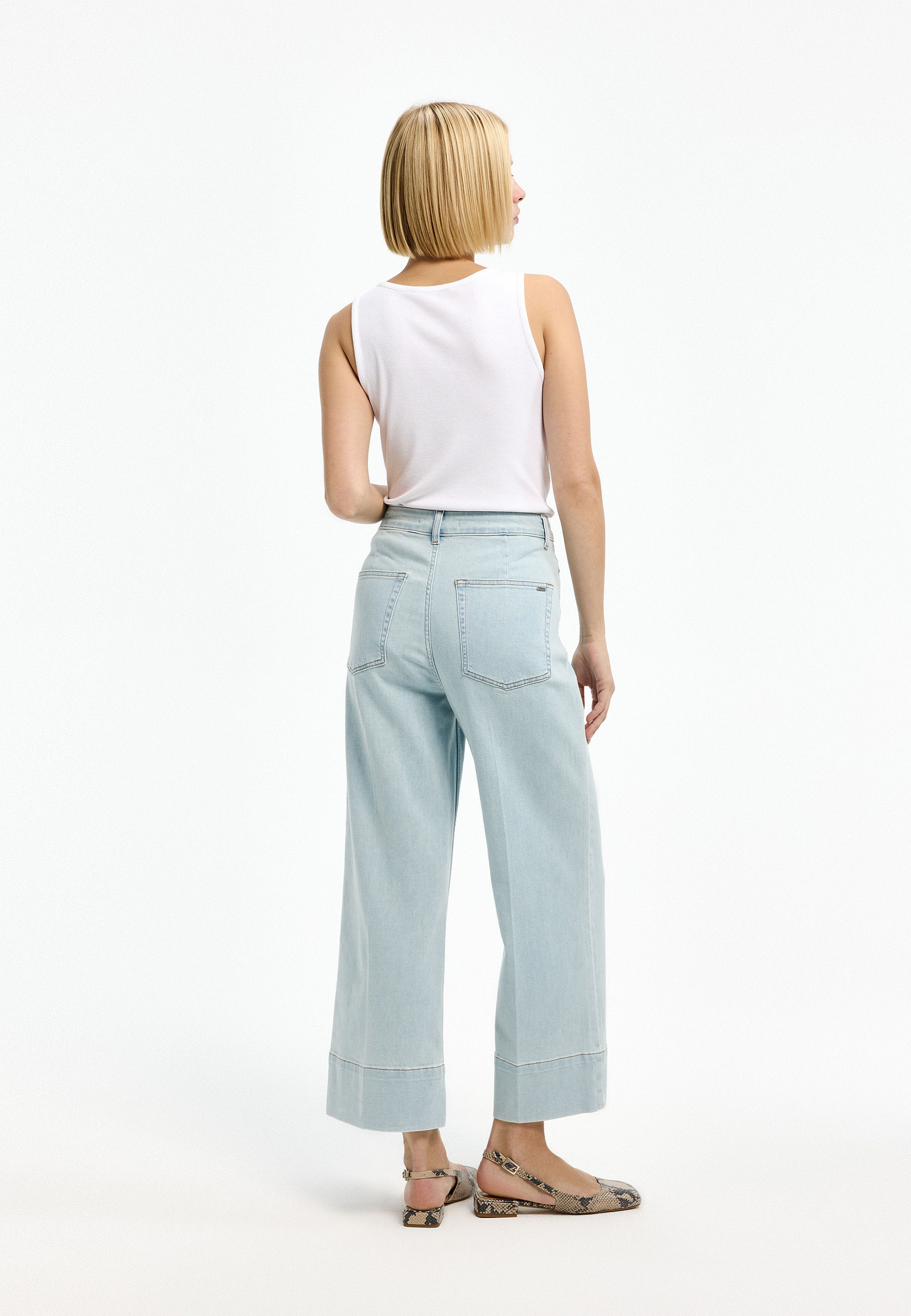 A woman wearing a white tank top and light blue wide-leg jeans.