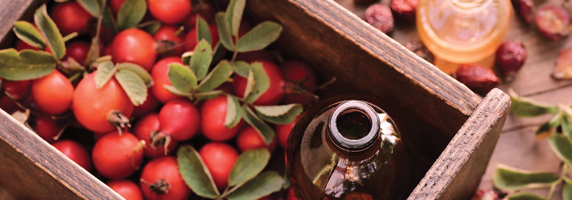 A wooden crate filled with small red fruits and a glass bottle.