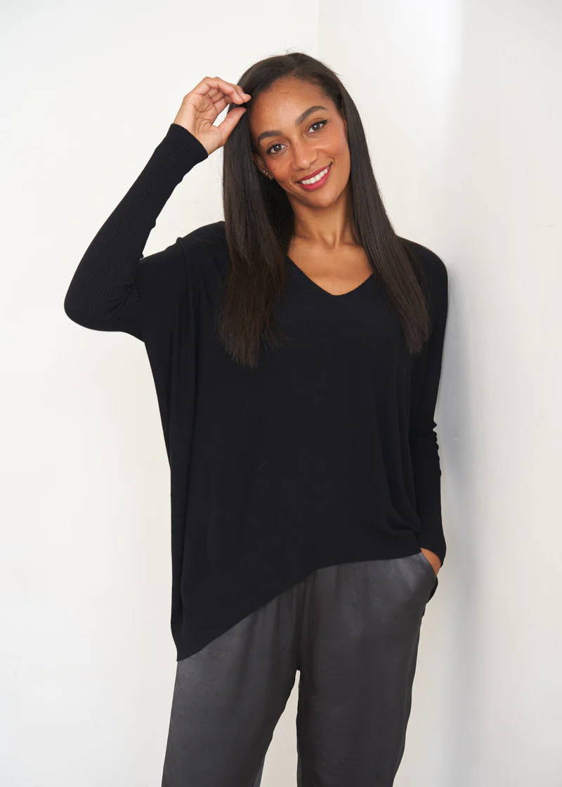 A model wearing a black slouchy jumper with fitted sleeves over dark grey trousers