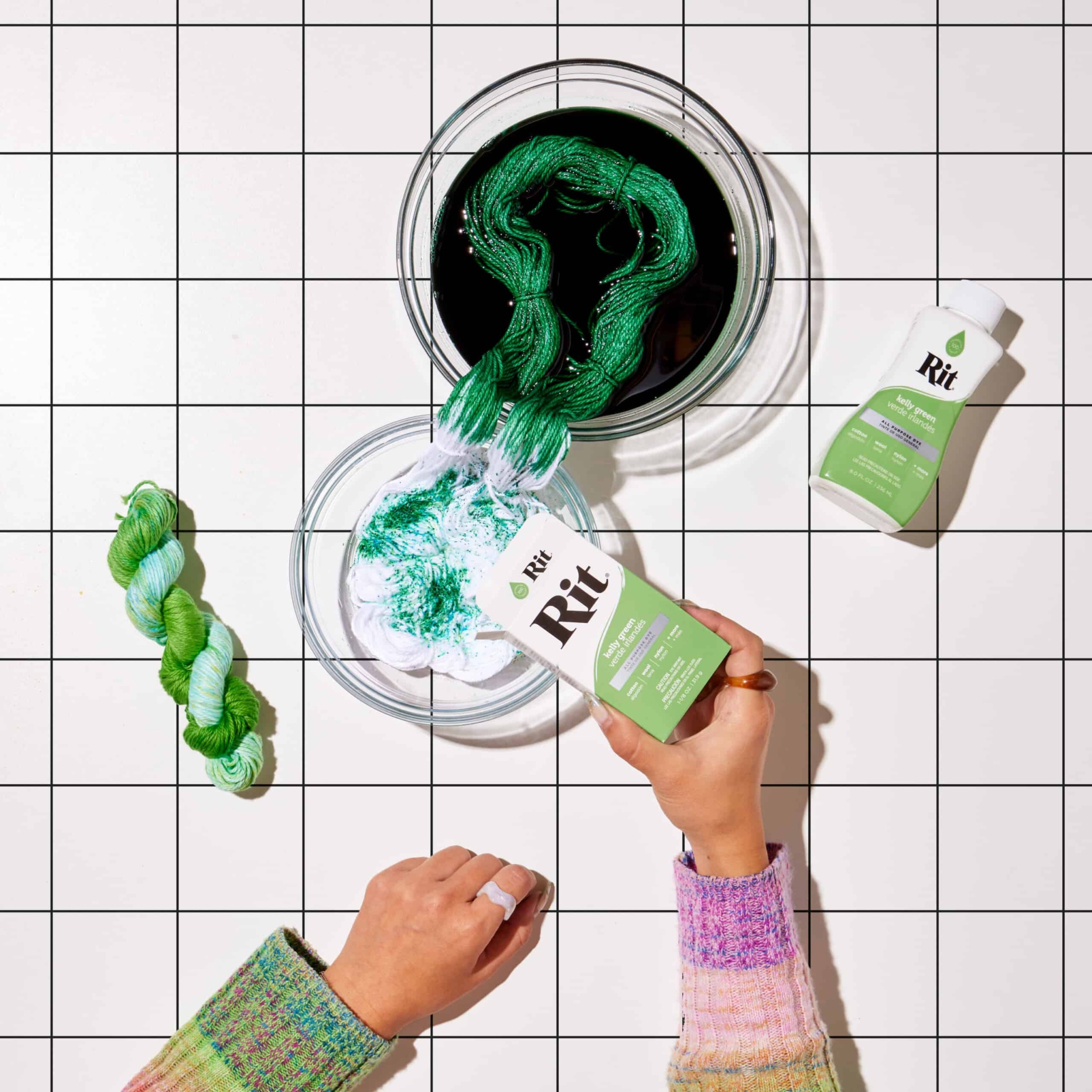 Hands pouring green dye into a bowl with a green yarn.