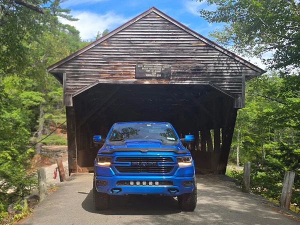 Blue RAM 1500 parked in front of historic wooden covered bridge in Albany