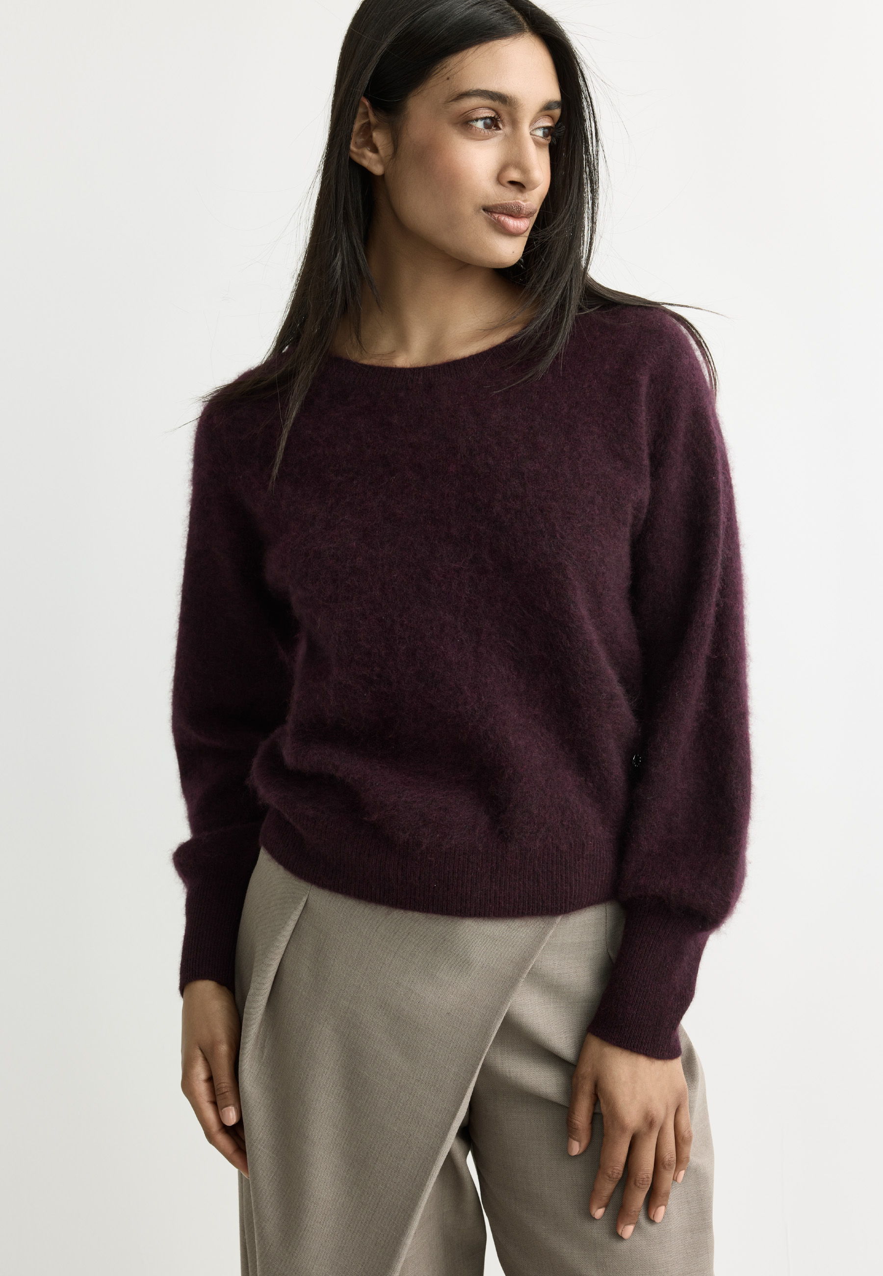 Woman wearing a burgundy sweater and beige pants, looking to the side.