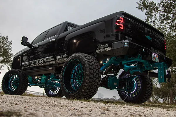 Low rear three-quarter view of Brandon's black 2018 Chevy Silverado 2500 with teal suspension and oversized custom wheels, install photo 5