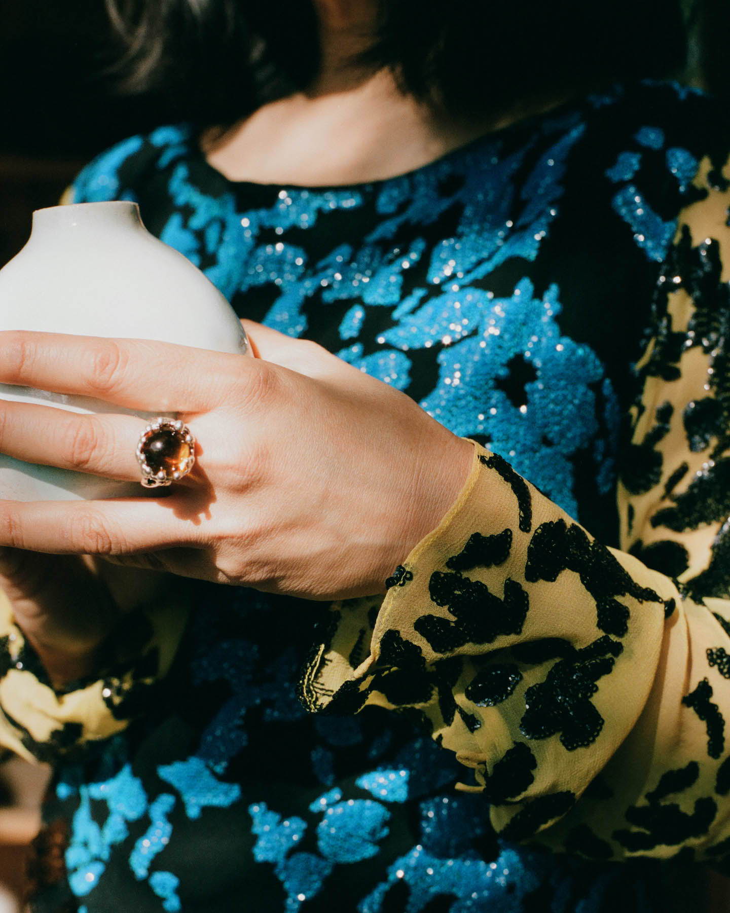 A close up image of Raina Lee holding a bud vase wearing a mondo mondo ring and Rachel Comey dress. 
