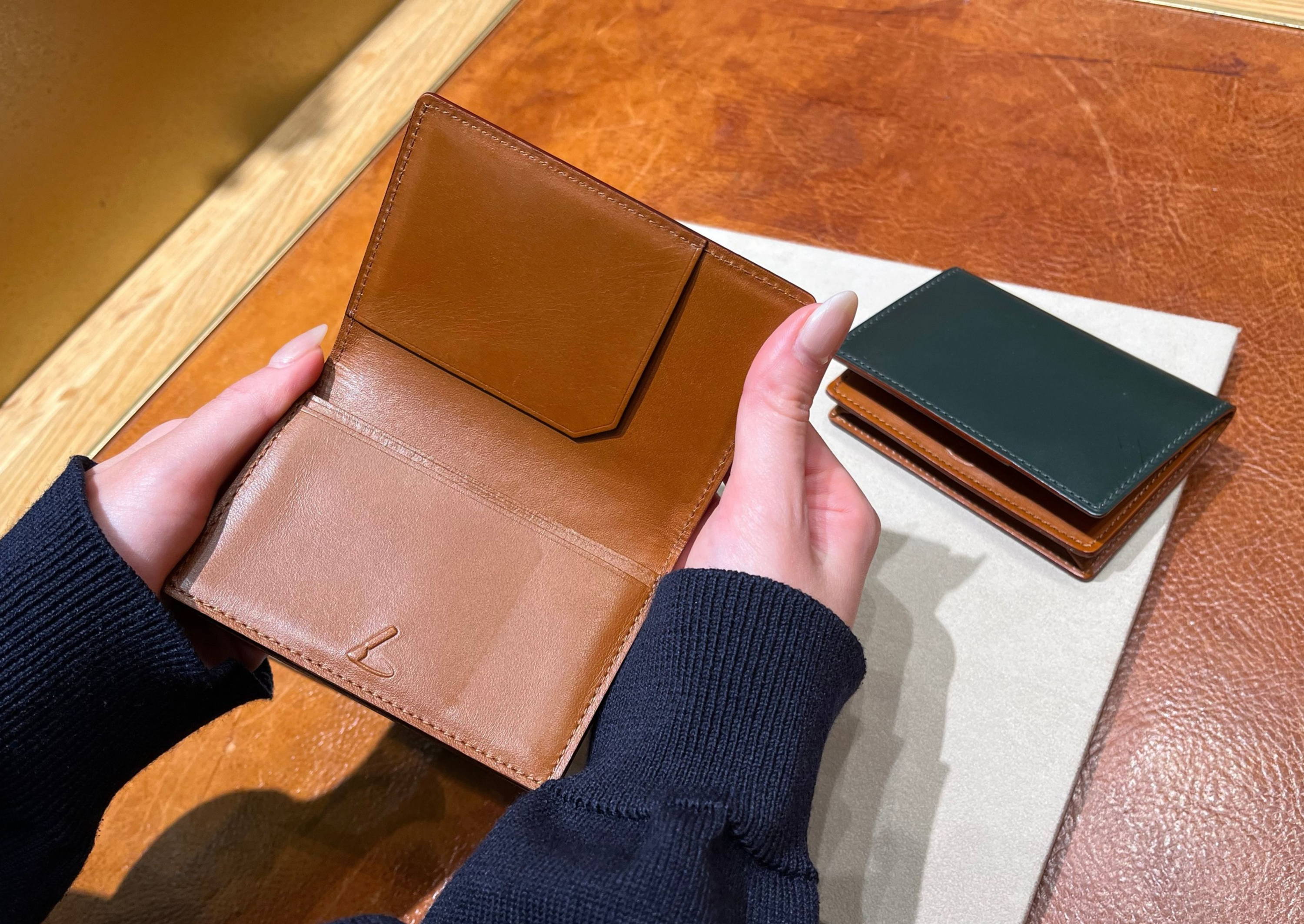 Person holding a brown wallet next to a green wallet on a surface.