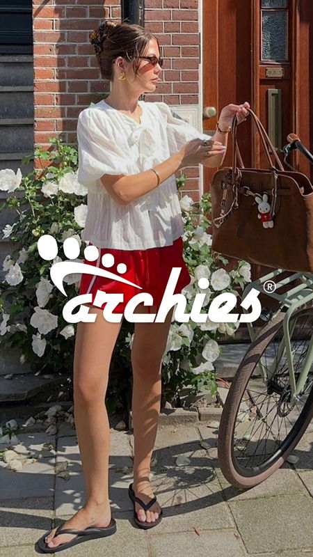 Woman in casual outfit holding a handbag near a bicycle and flowers.