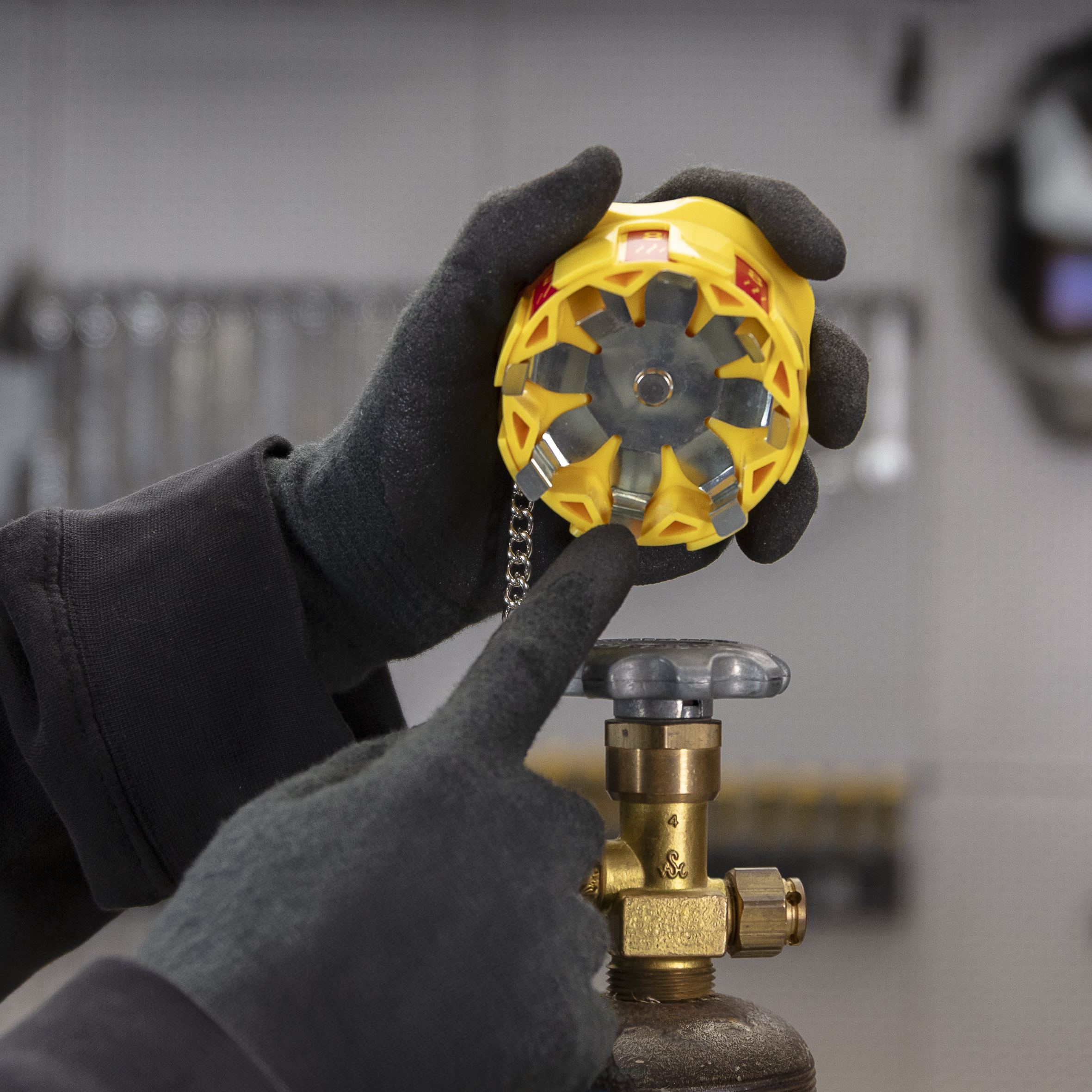 Person in gloves pointing at a yellow device near a valve.
