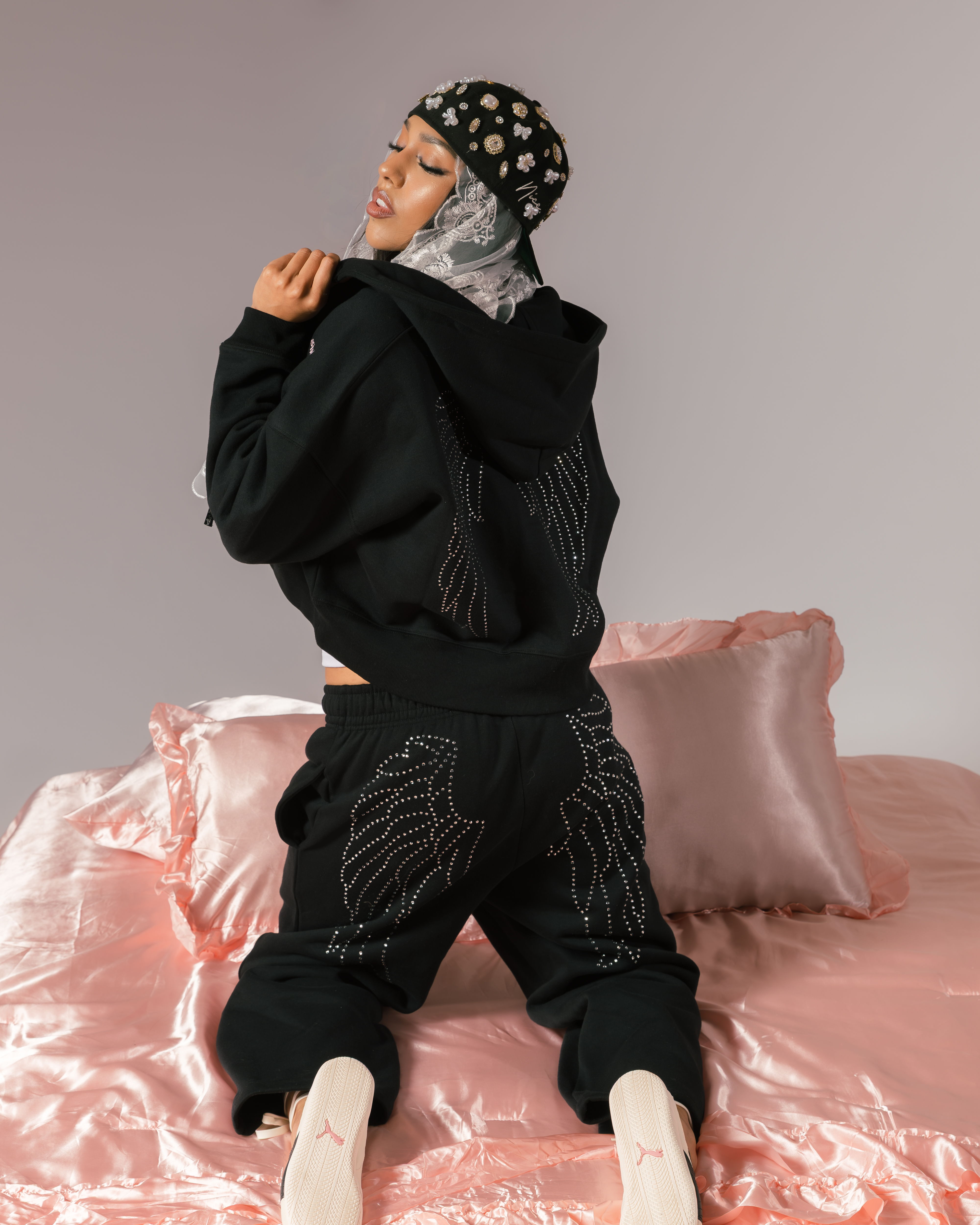 Person in black outfit poses on a pink satin bedspread.