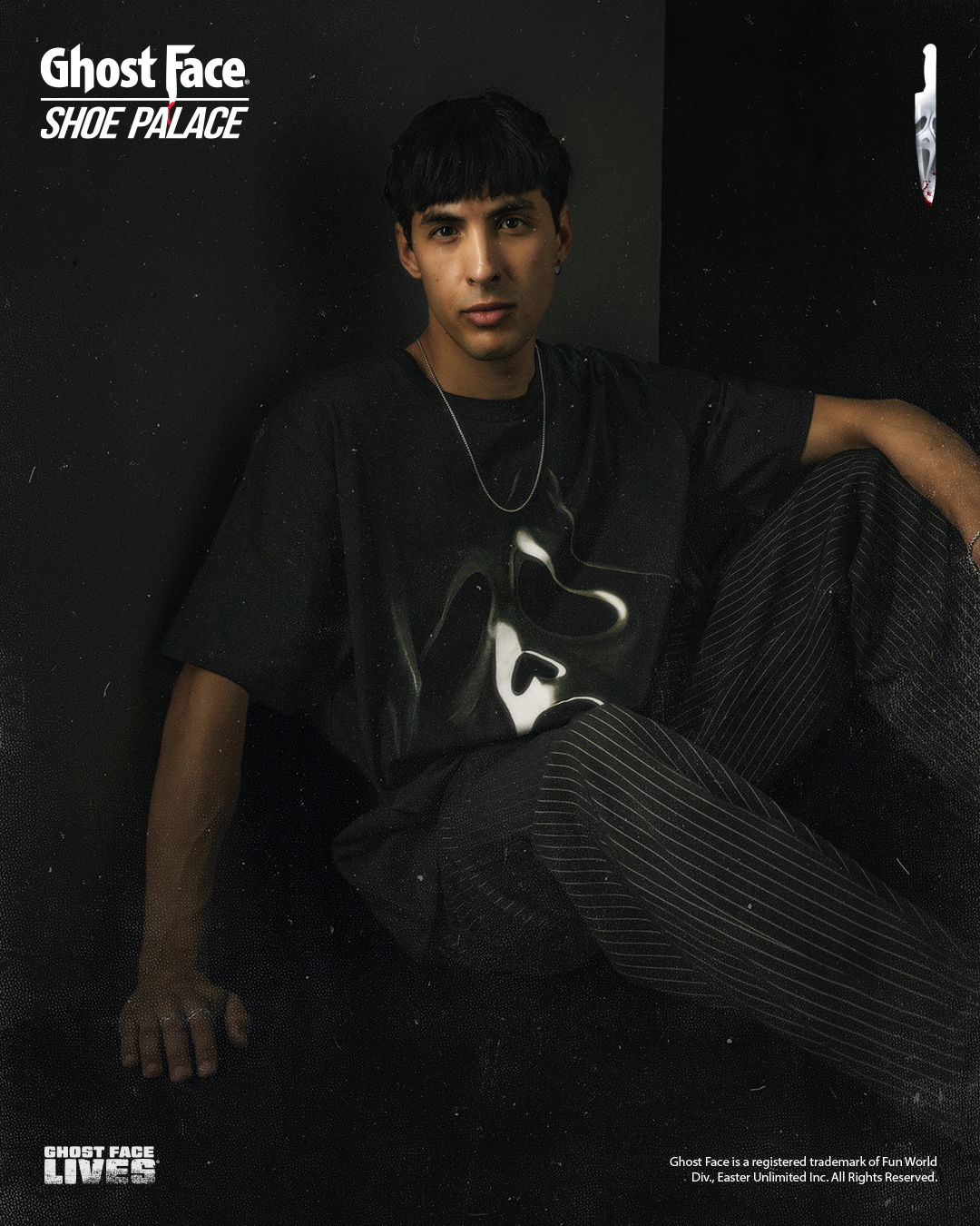 Person sitting against a wall, wearing a graphic t-shirt and striped pants.