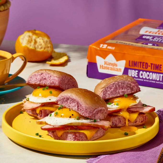 Three ube coconut sandwiches on a yellow plate with a cup and orange.