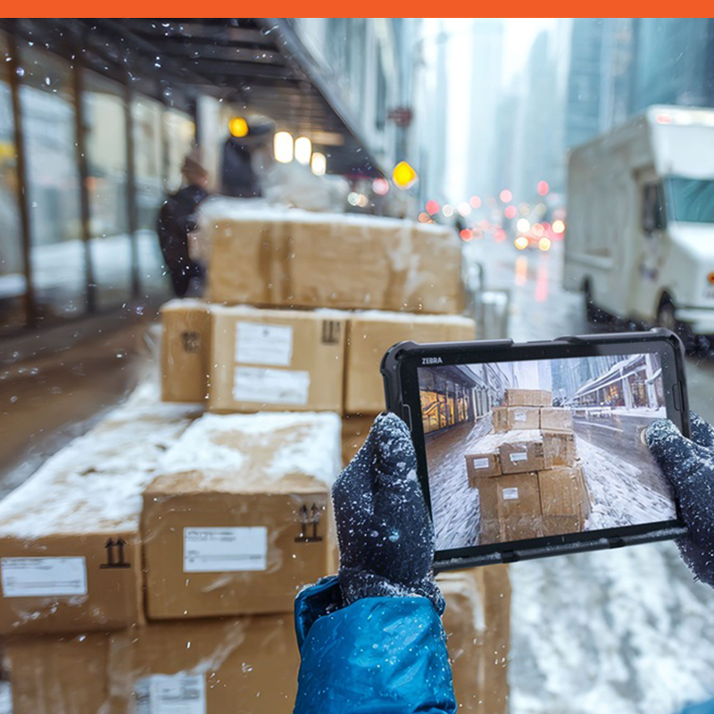 Person holding a tablet, photographing stacked boxes in a snowy urban environment.