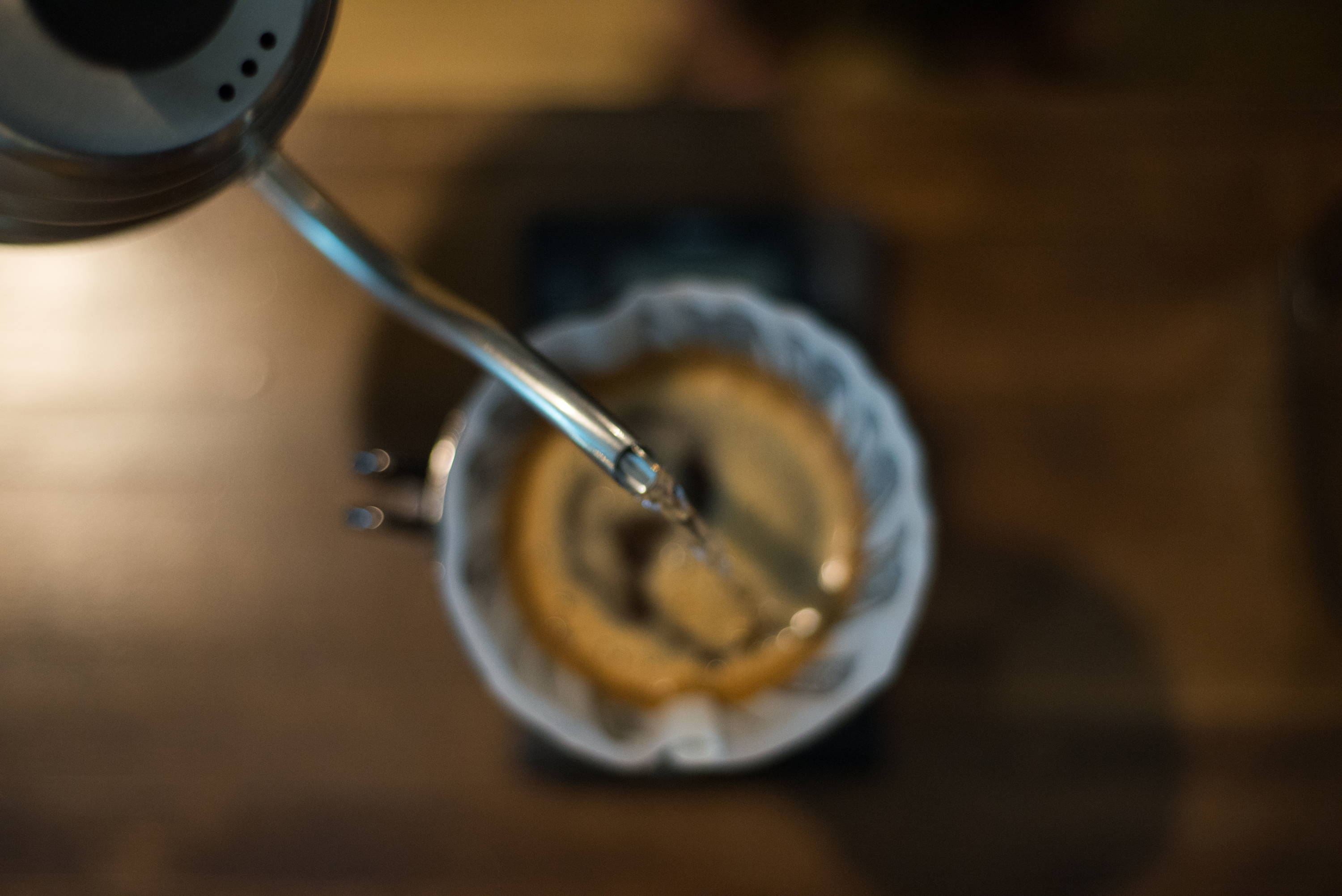 Top shot of a kettle pouring water into a V60 brewer filled with coffee grounds on a wooden surface