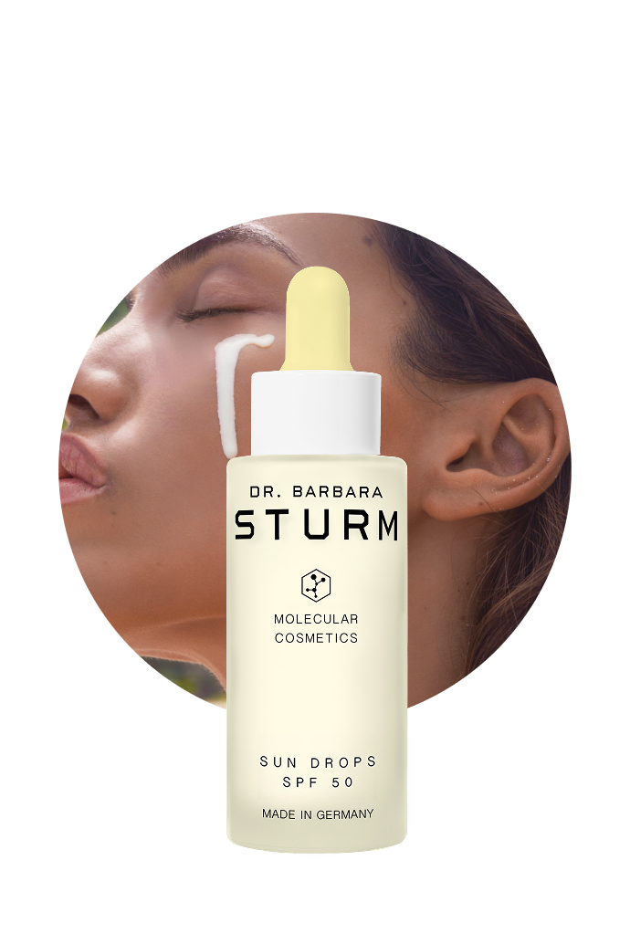 Bottle of Dr. Barbara Sturm Sun Drops SPF 50 with model applying it.