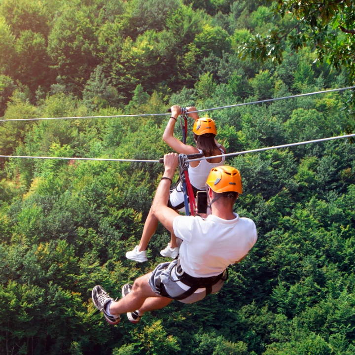 Two people ziplining over a forest