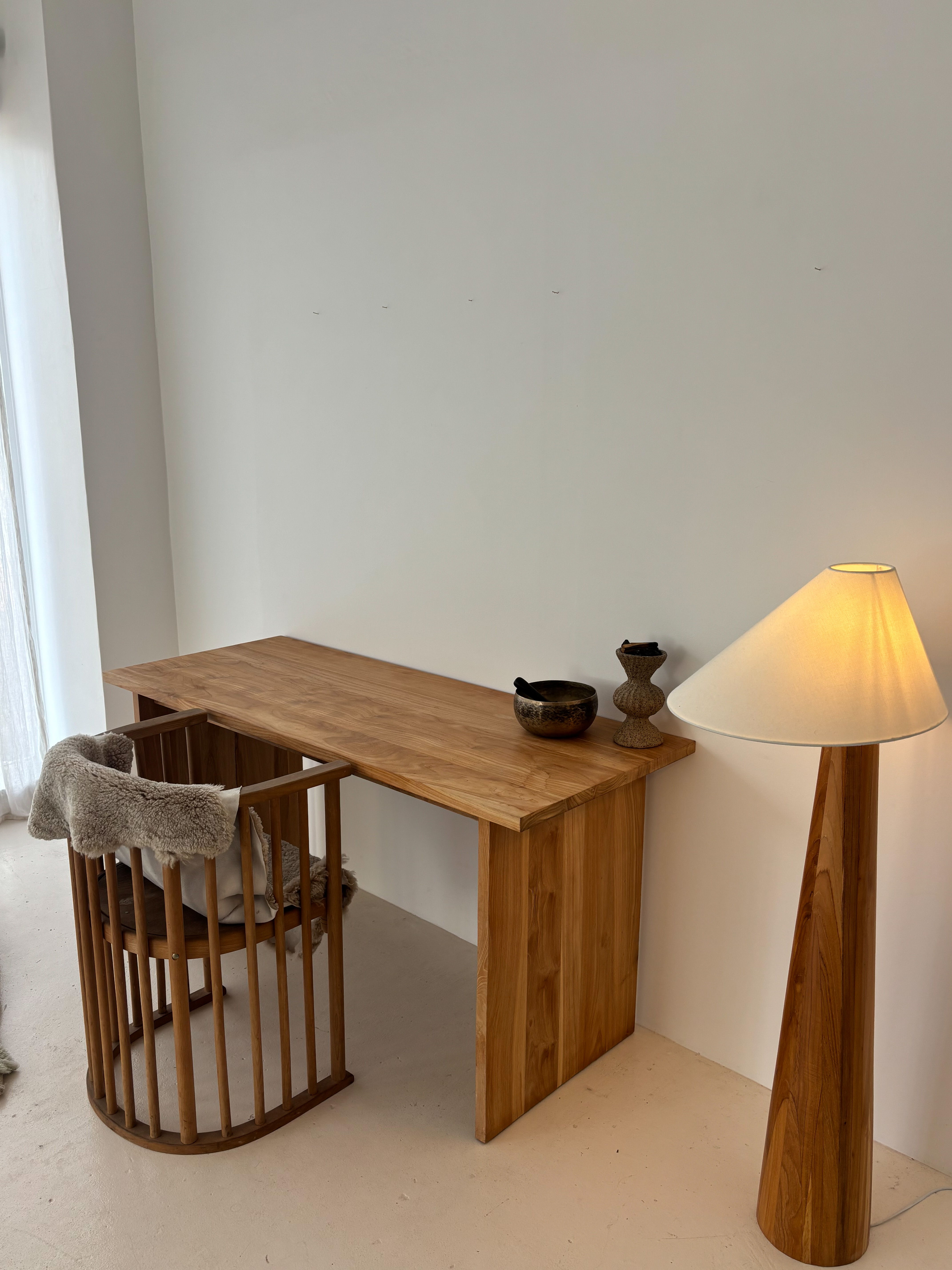 A wooden desk with a chair and a lamp in a minimalist room.