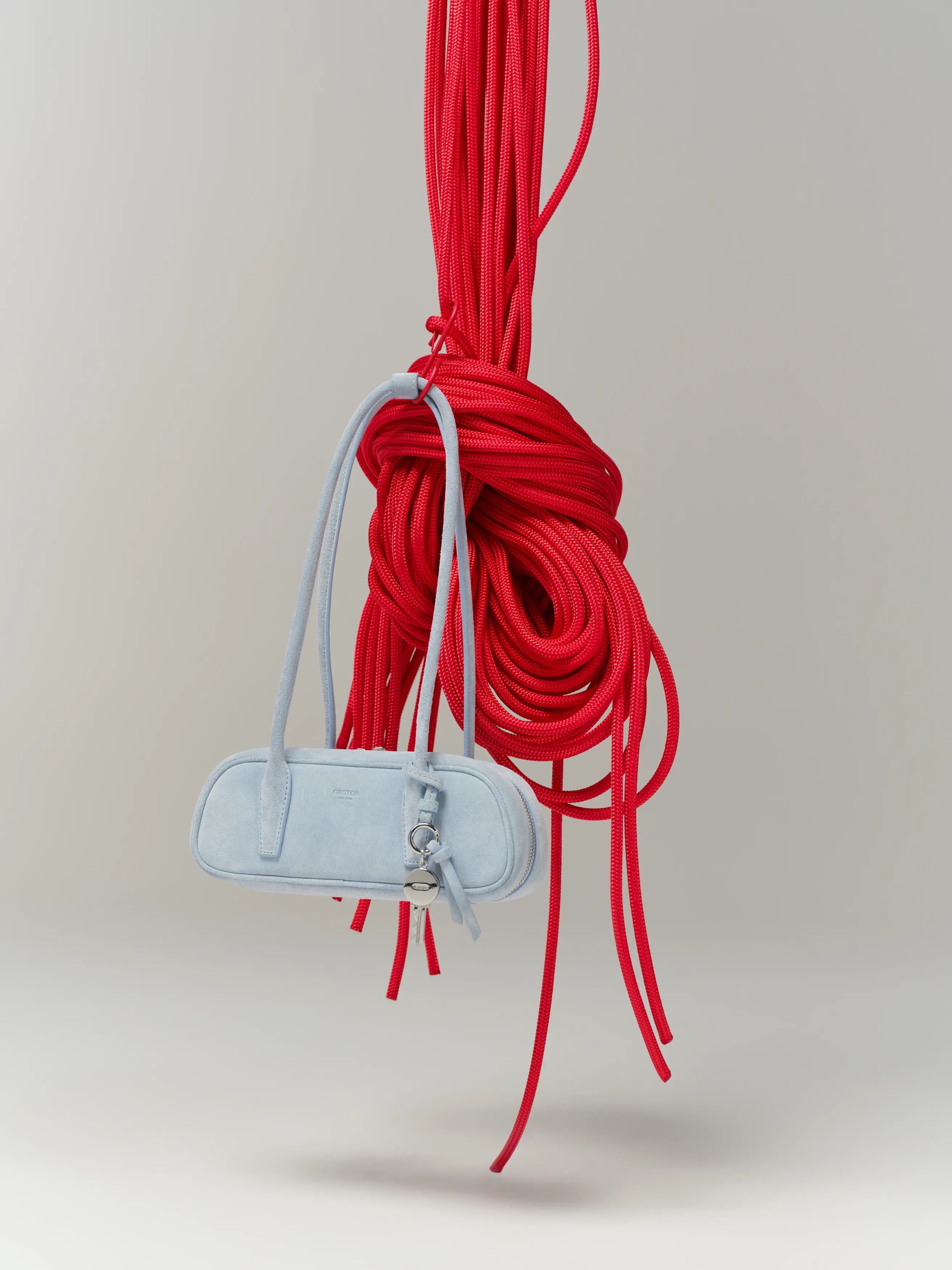 A light blue handbag hanging from a knotted red rope.