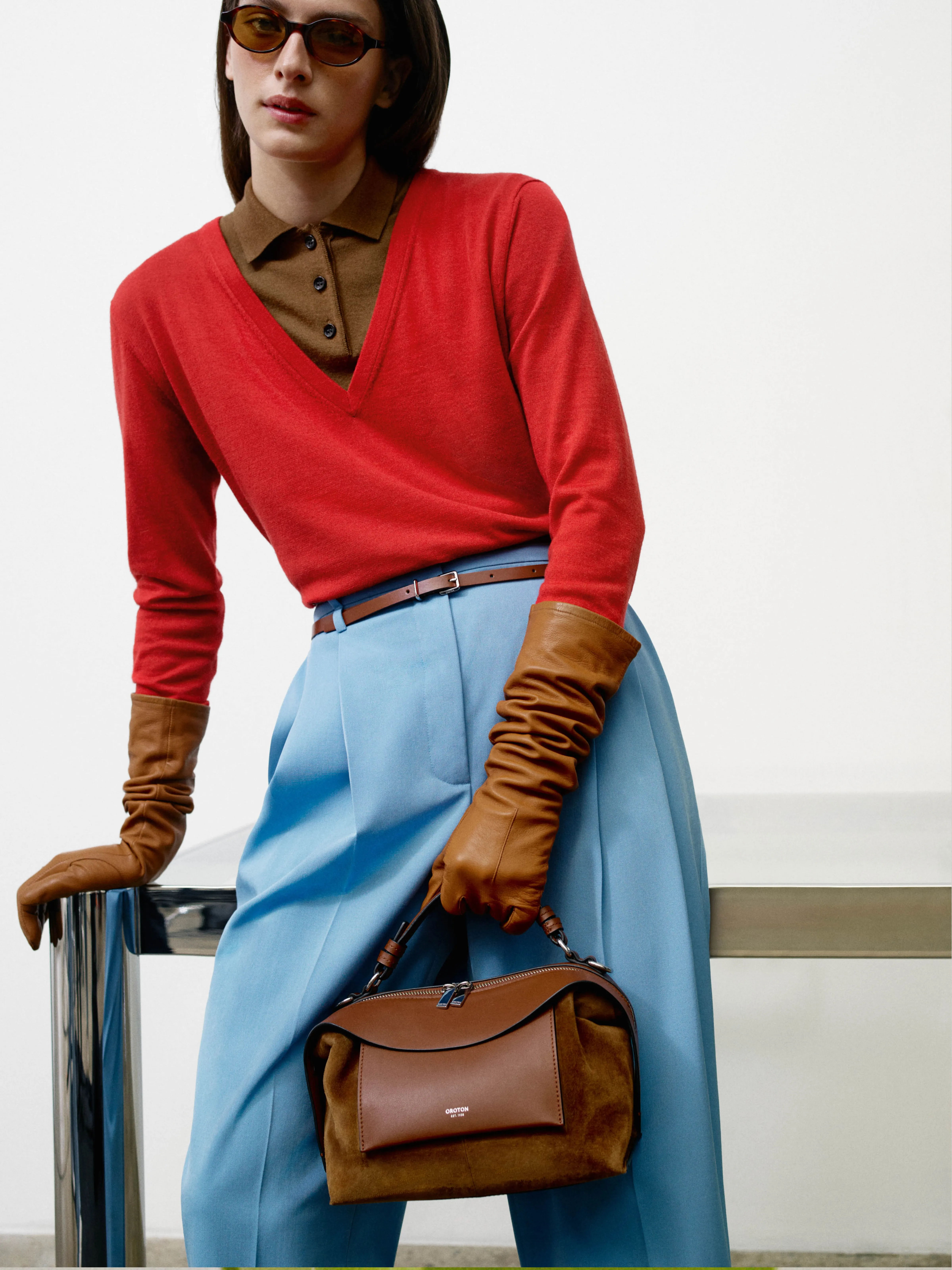 Person in stylish outfit with red sweater, blue pants, and handbag.