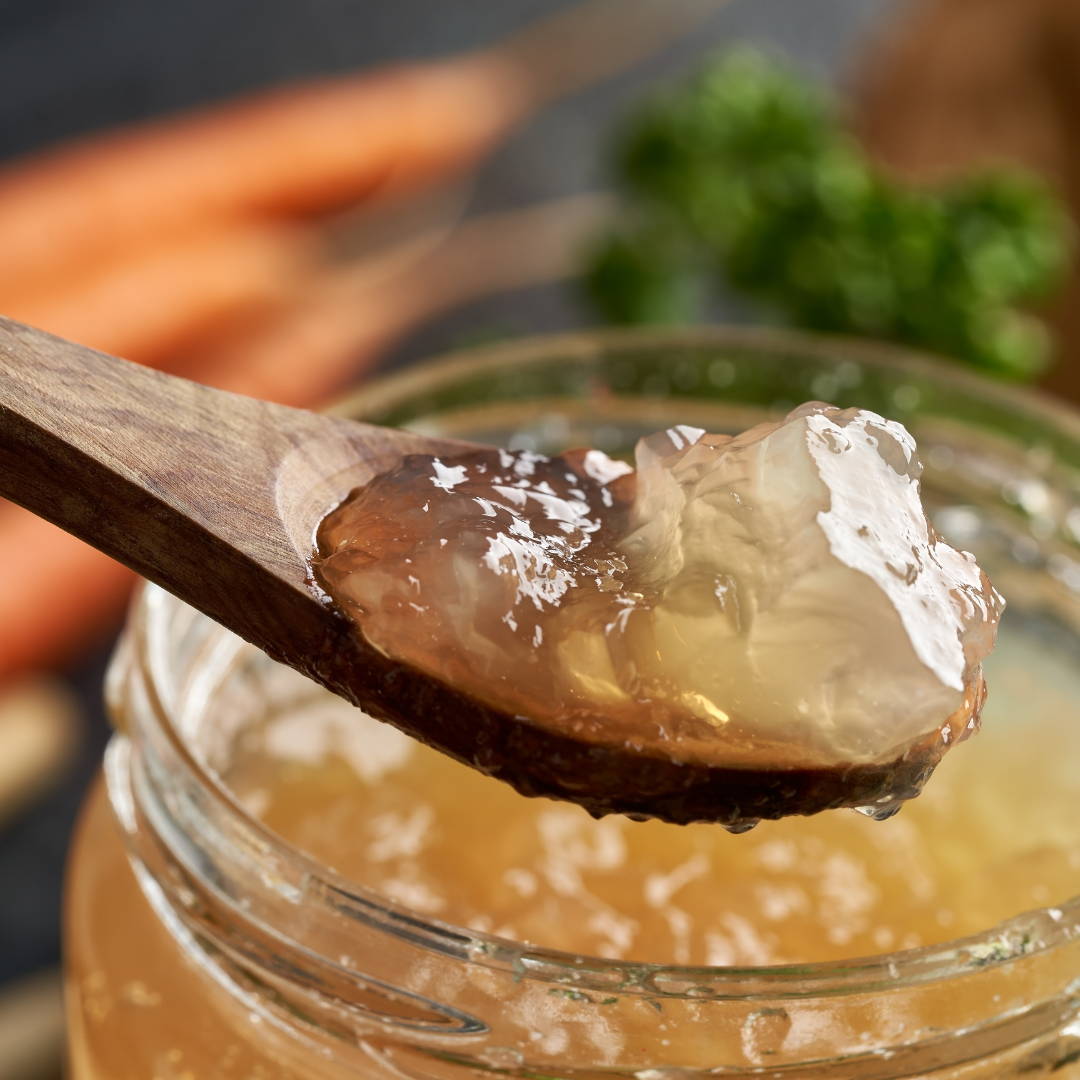 Thick bone broth in wooden spoon over glass mason jar of broth.