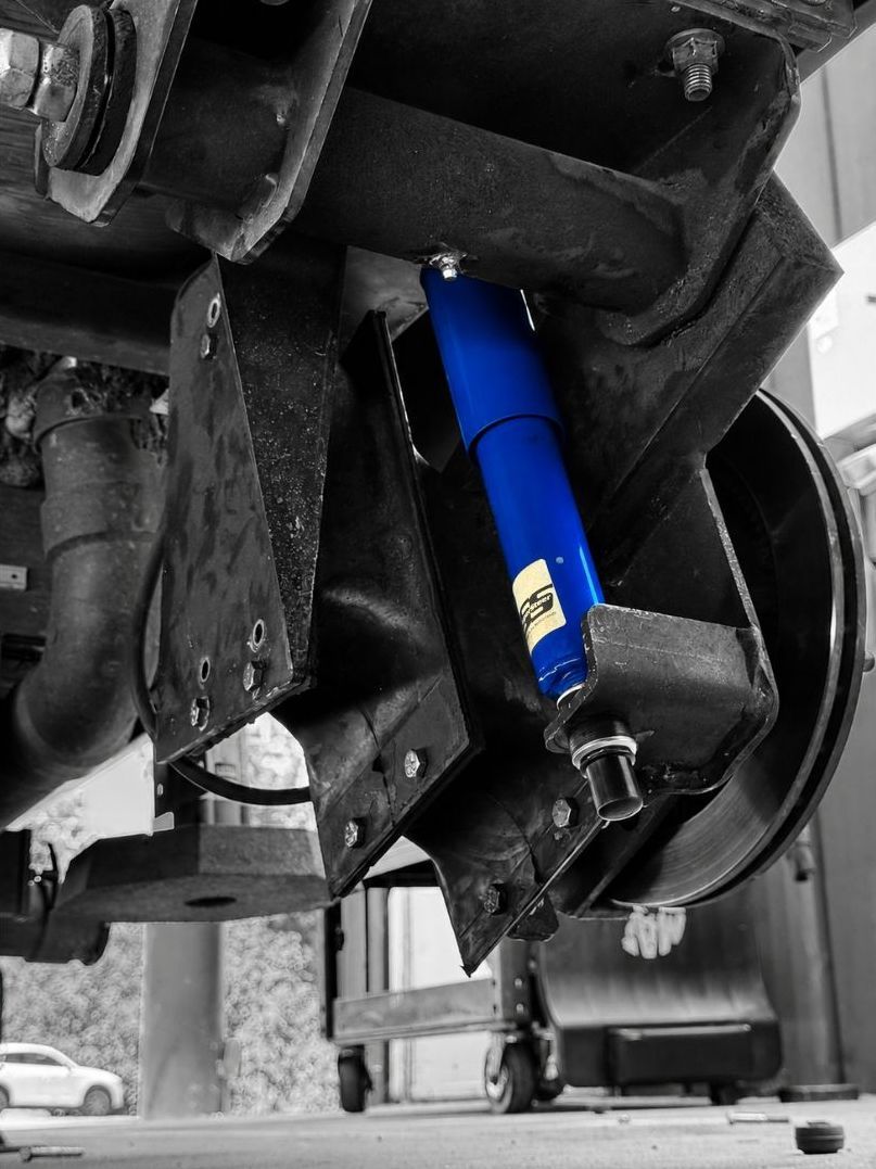 A blue shock absorber mounted under a vehicle, with a monochrome background.