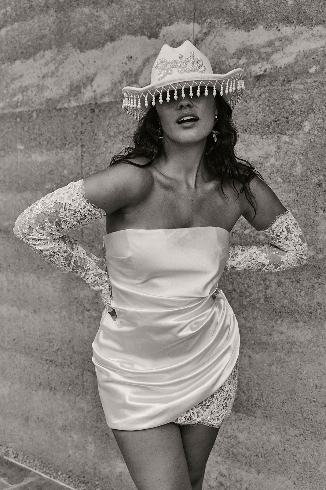 A woman in a strapless dress and hat poses confidently.