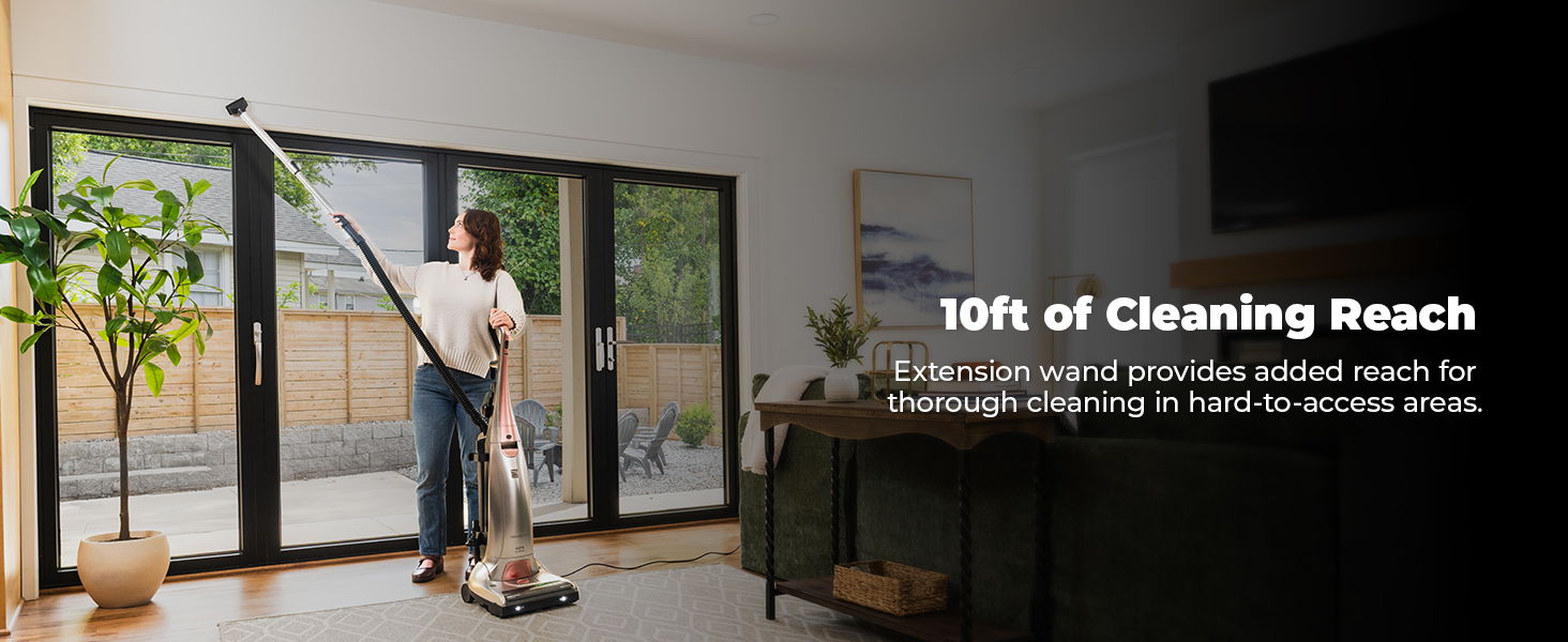 Woman using a vacuum cleaner in a bright, modern room with large windows.