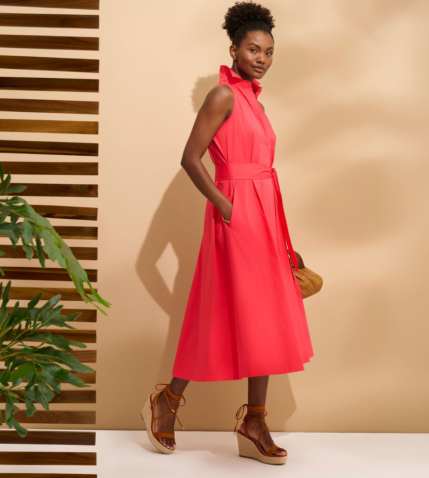 Woman in a pink dress standing next to a plant and wooden backdrop.