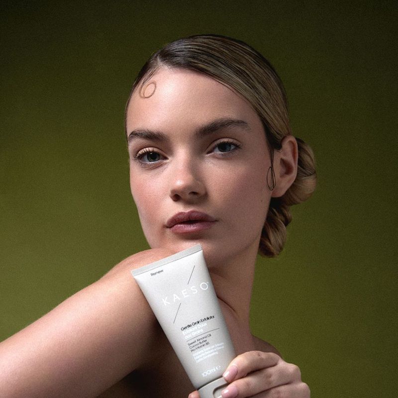 A model holding a skincare product against a green background.