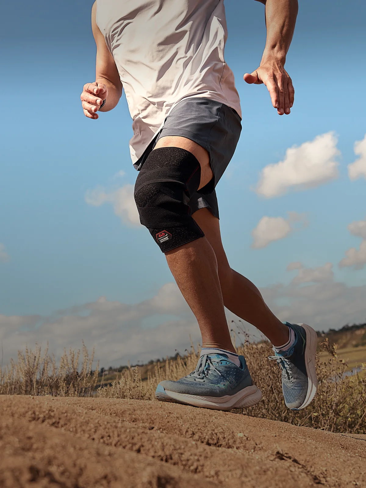 Person running on a dirt path, wearing a knee brace and athletic shoes.
