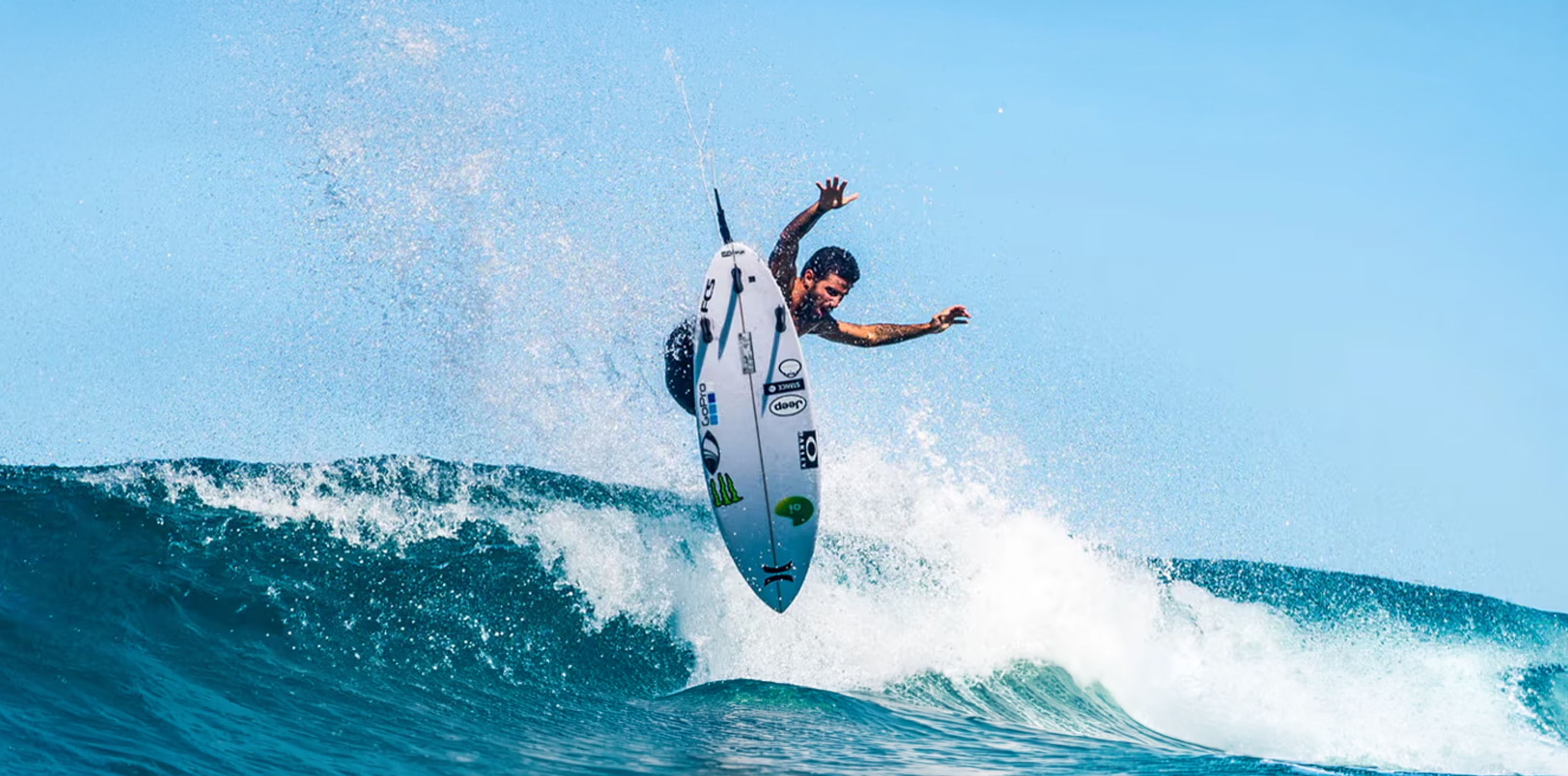 A surfer performing a trick on a wave under a clear blue sky.