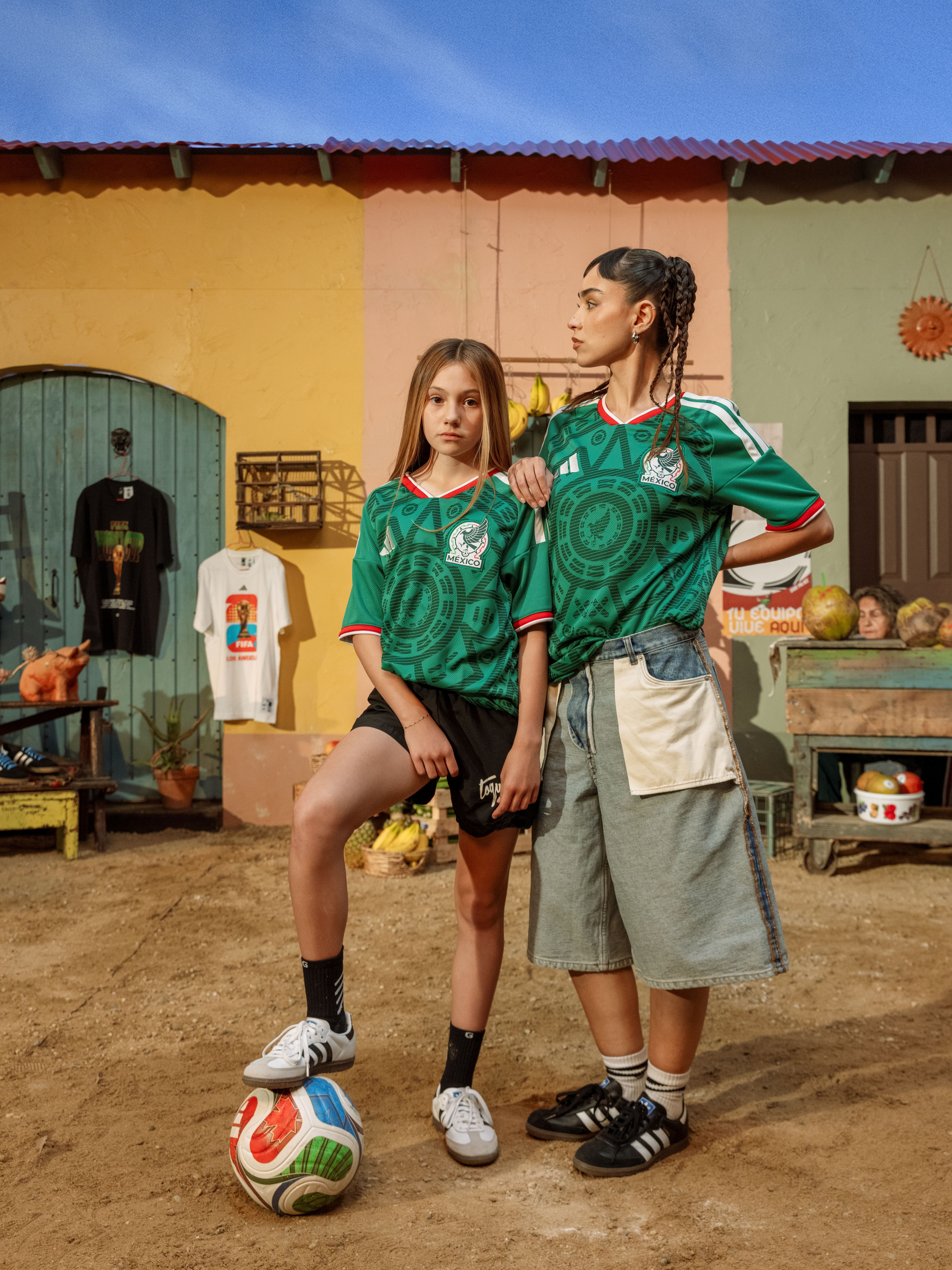 Two girls in soccer jerseys pose with a ball in a colorful setting.