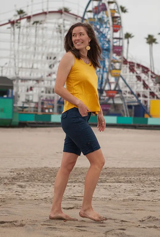 Smiling woman in yellow top and shorts walking on the beach.