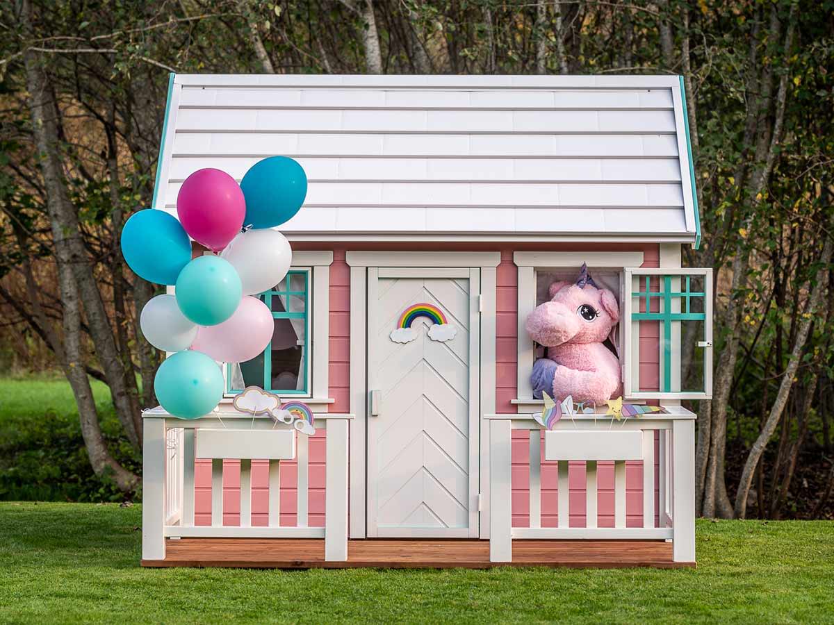 Pink wooden playhouse Unicorn with a white porch and decorations with forest background by WholeWoodPlayhouses