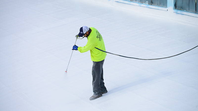 Worker spraying AMES roof white Blue Max roof product