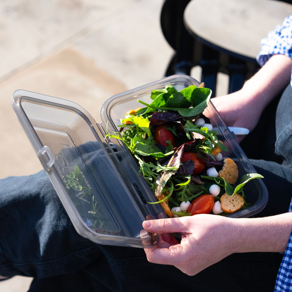 A person holding a transparent container filled with fresh salad ingredients.