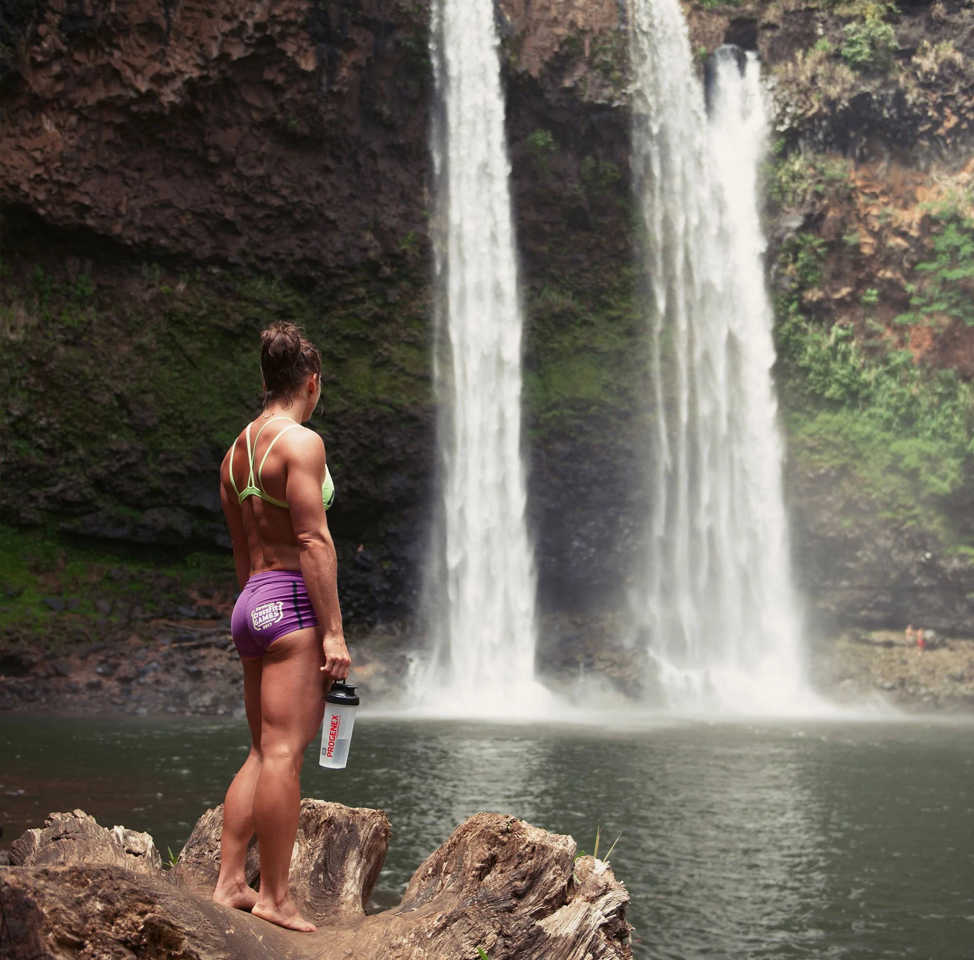 Woman standing in front of falling waterfall with PROGENEX shaker in hand