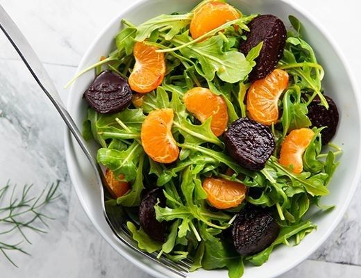 A bowl of mixed greens with mandarin slices and roasted beets.