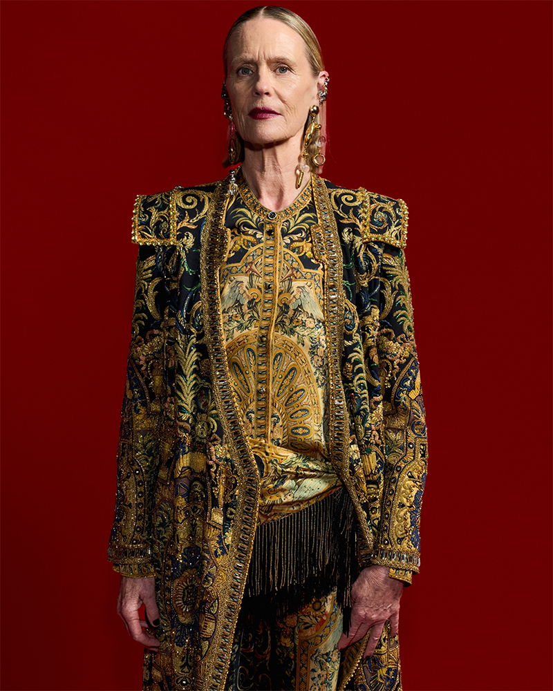 A woman in a richly detailed, ornate outfit against a red background.