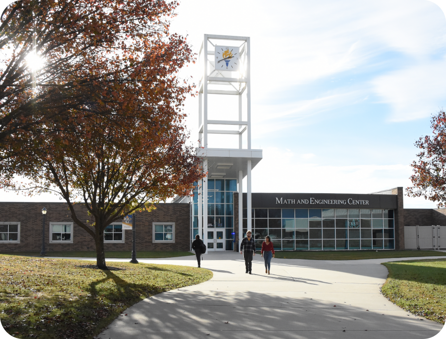 Three people walking towards a modern building with trees nearby.