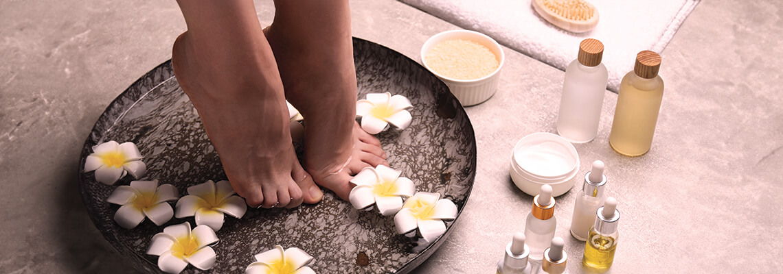 Feet in a bowl with flowers, surrounded by beauty products.