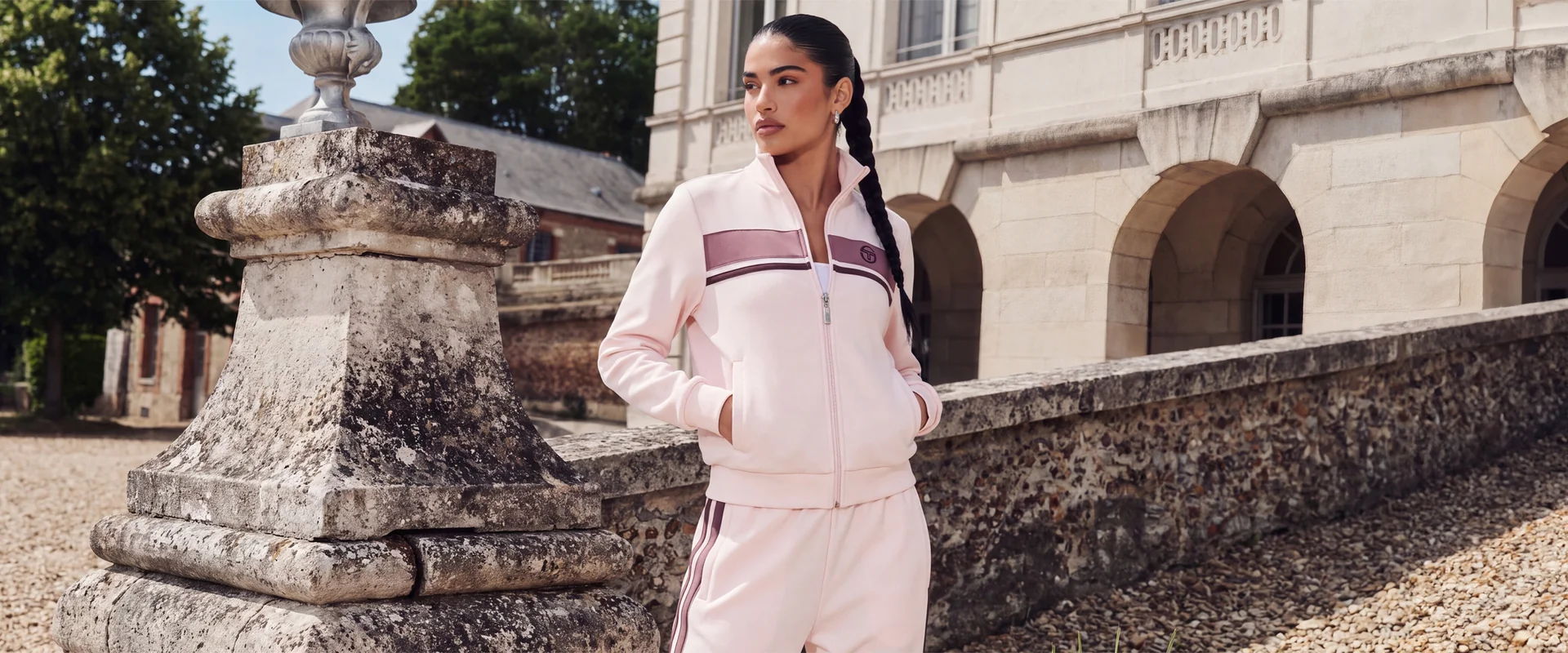 Woman in pink Sergio Tacchini tracksuit standing by a stone wall outside.